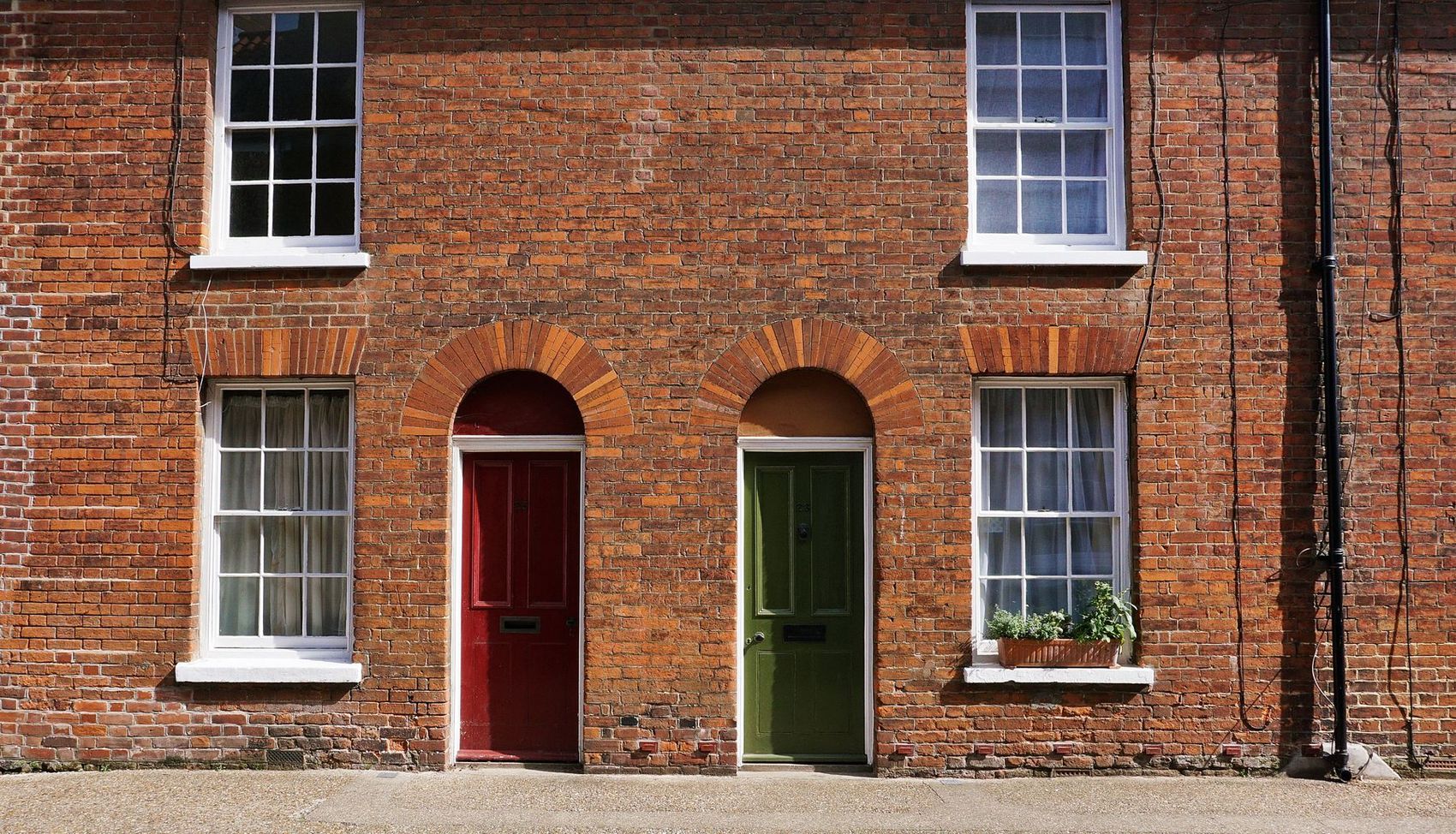 A red and a green front door side by side on a red brick terrace