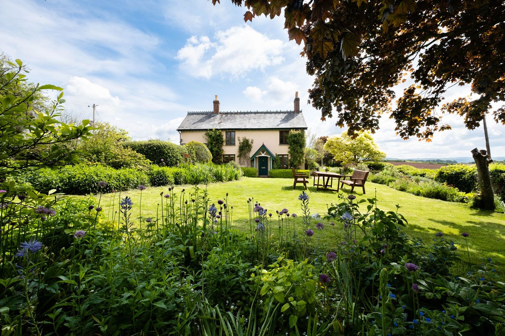 A cream-rendered cottage behind a long summer garden, with new windows and a green front door