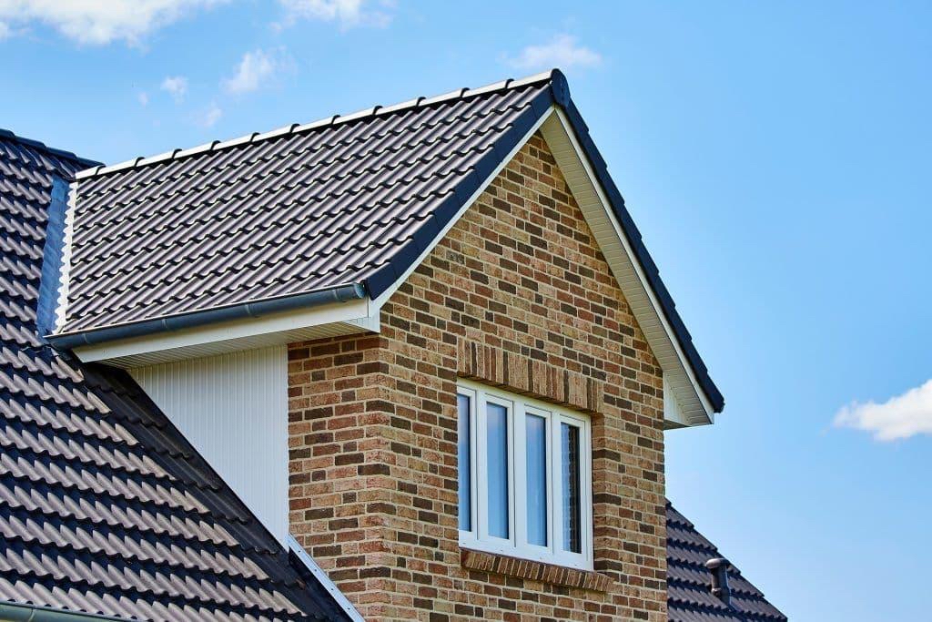 Grey tiled roof with verge edging, ridge tiles, white soffits and guttering on a brick house