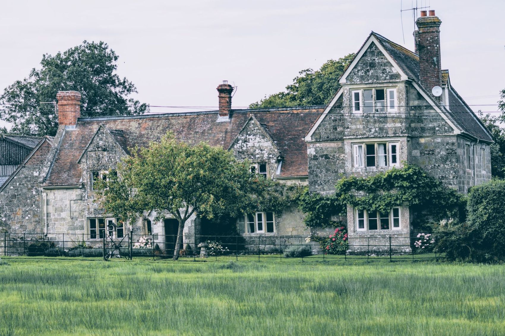 An English stone manor house with tall windows and a lawn